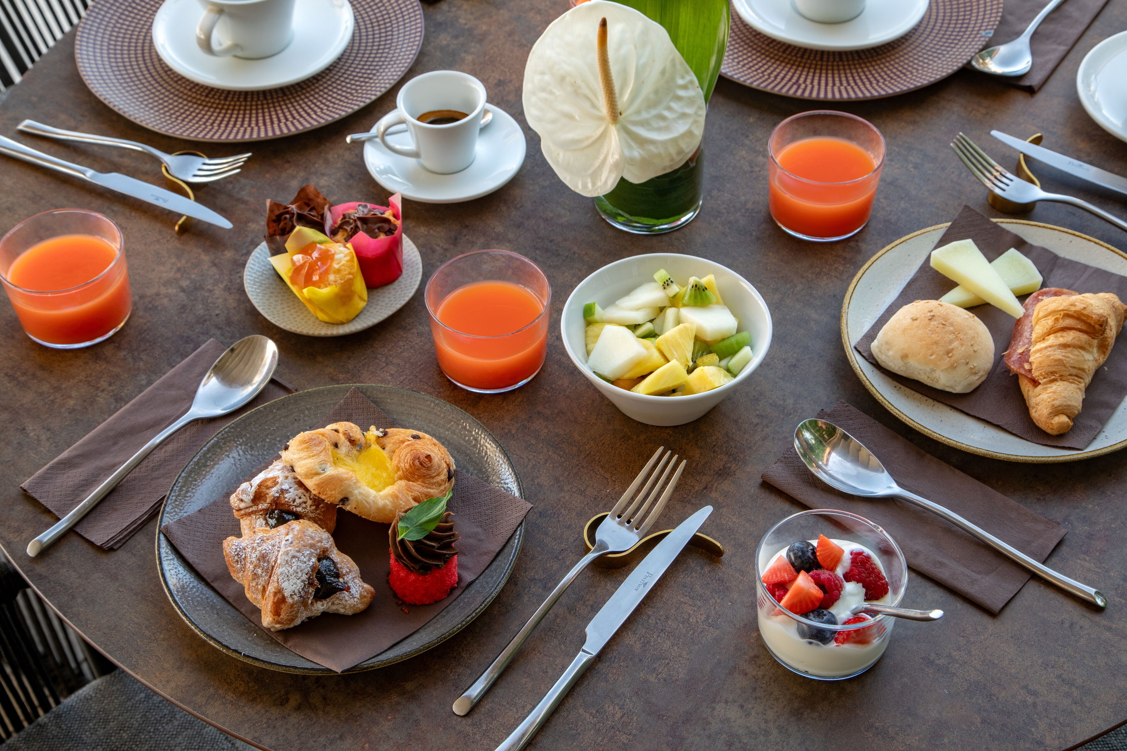 Une table dressée pour le petit-déjeuner, avec des croissants, des fruits et des boissons.