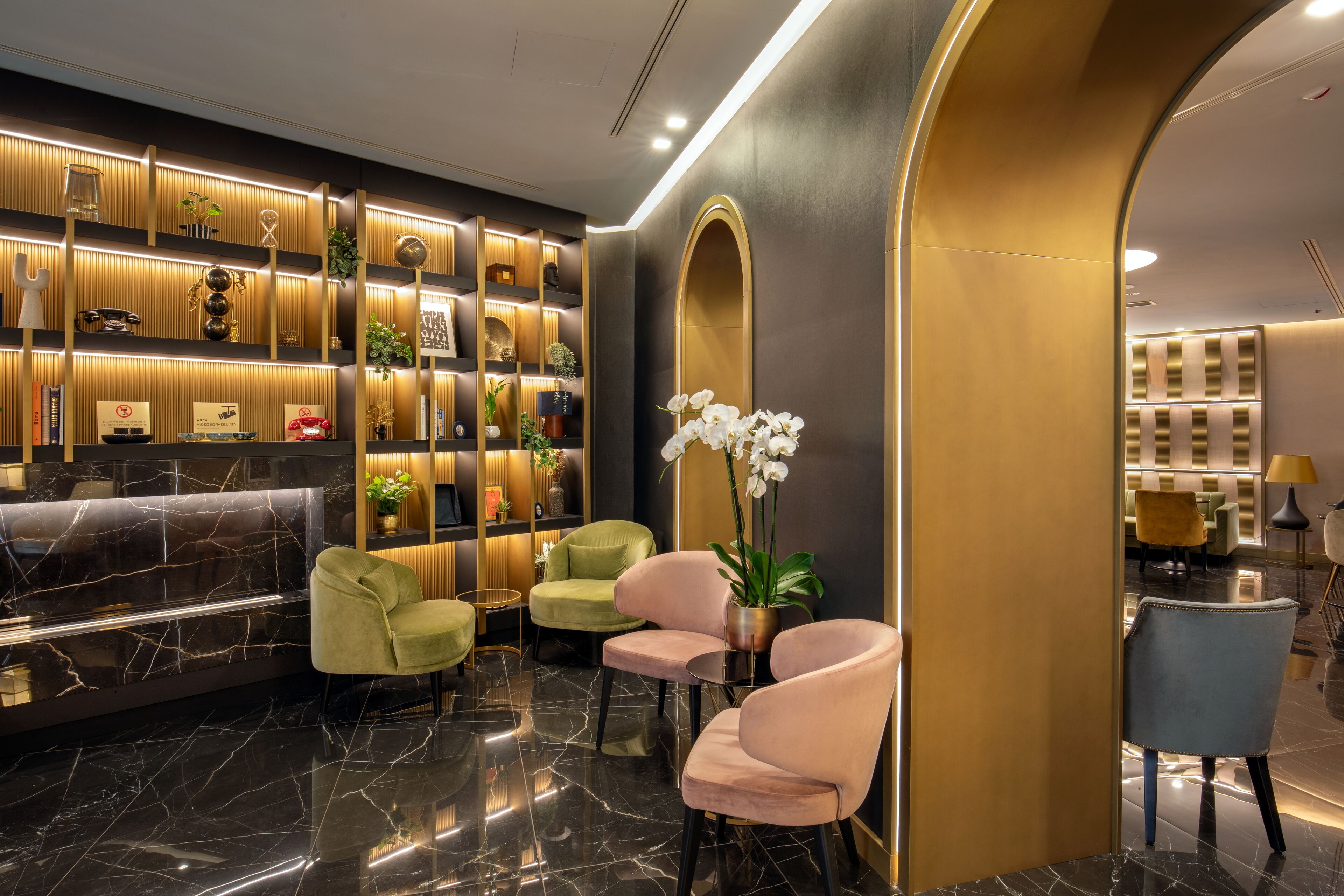 A modern lobby with a marble reception desk, plush seating, and a decorative wall with plants and shelves.
