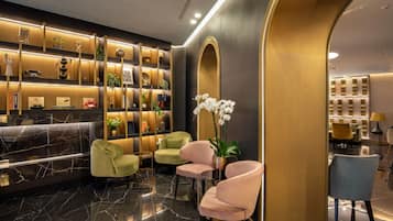 A modern lobby with a marble reception desk, plush seating, and a decorative wall with plants and shelves.