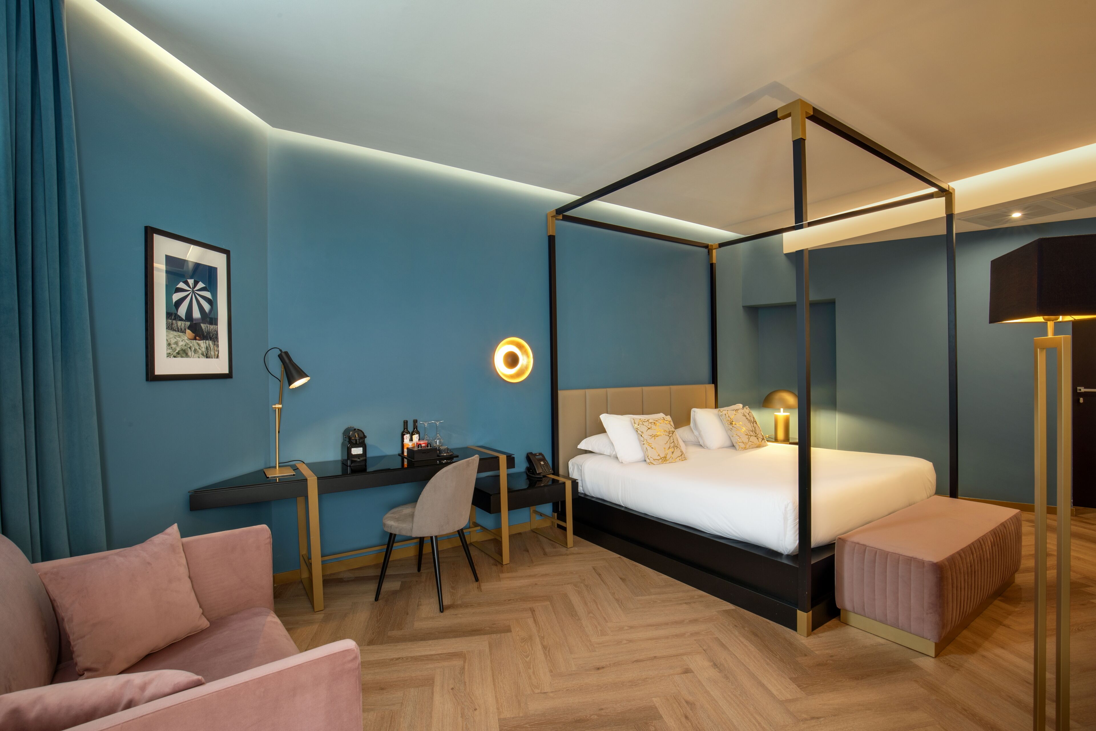 Une chambre d’hôtel moderne avec un lit à baldaquin, un bureau avec une chaise, un petit canapé et une table de chevet avec une lampe.
