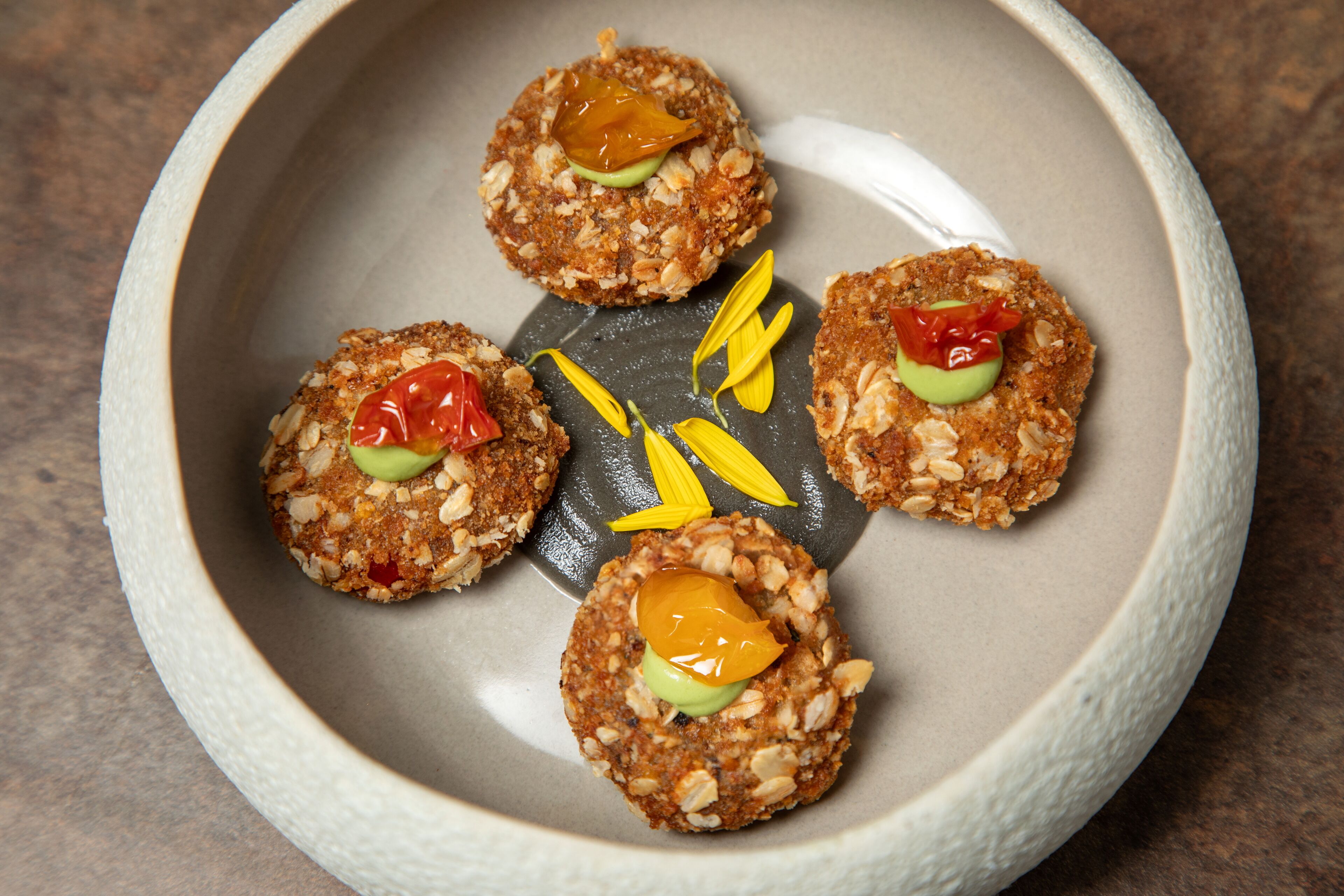 A plate with four food items, each topped with a slice of avocado and a piece of fruit.