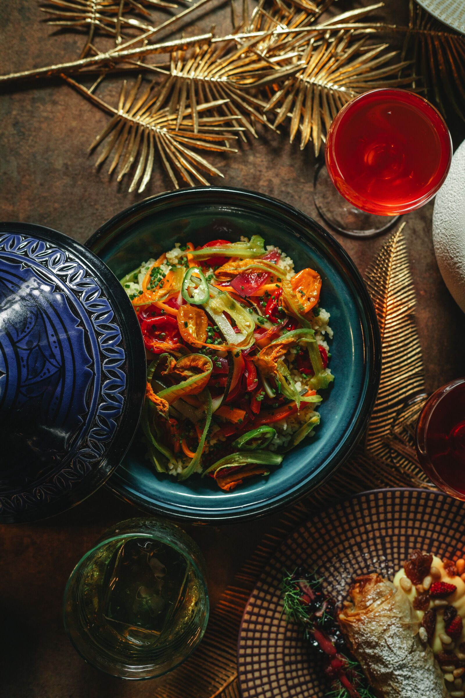 Uma mesa com uma saladeira azul, um copo de vinho tinto e um prato decorativo com comida.