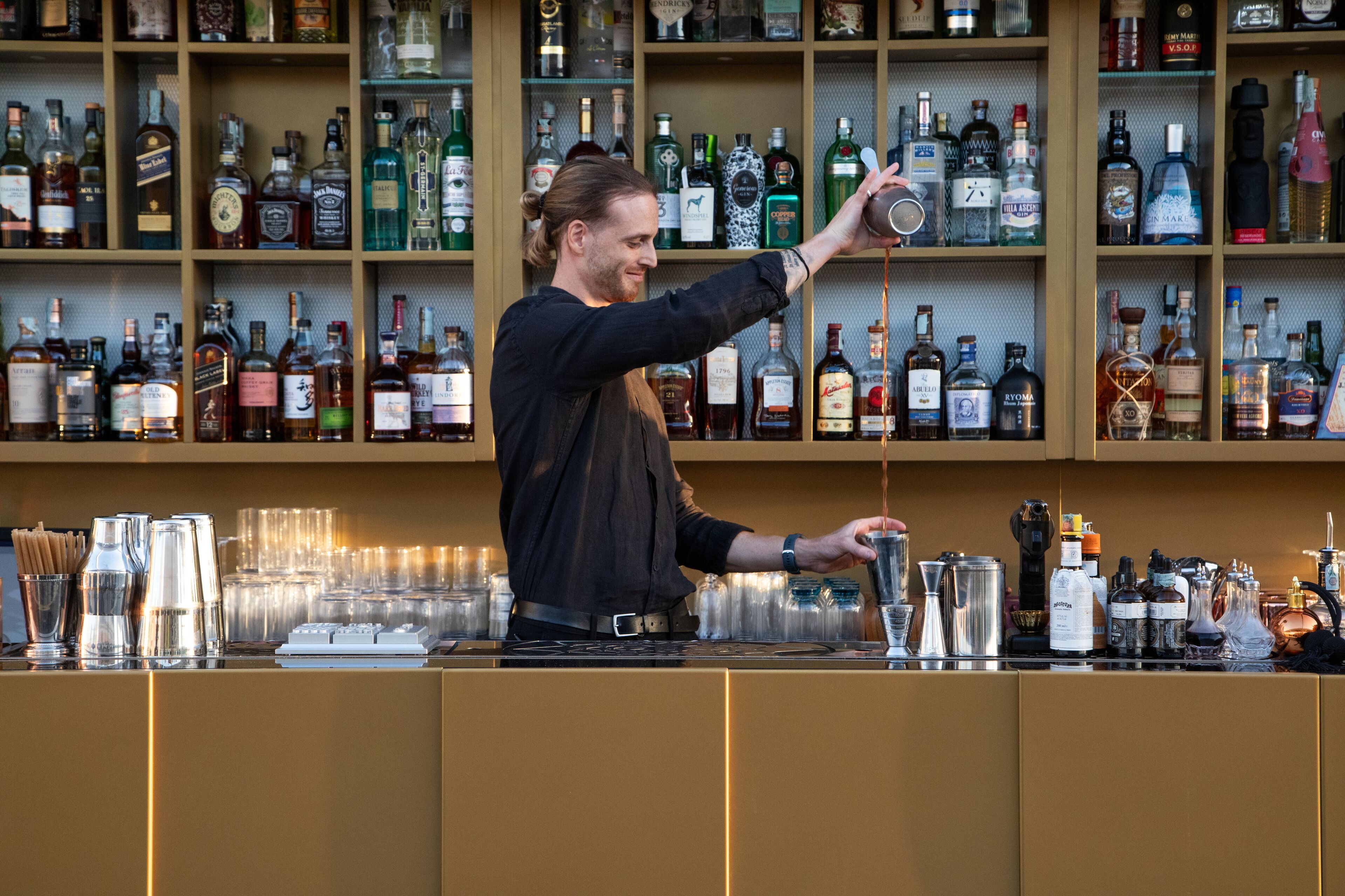 Un bar con scaffali pieni di bottiglie di liquore e un barista che prepara un cocktail.
