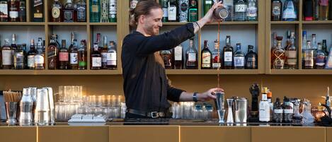 Un bar con estantes llenos de botellas de licores y un barman preparando una bebida.