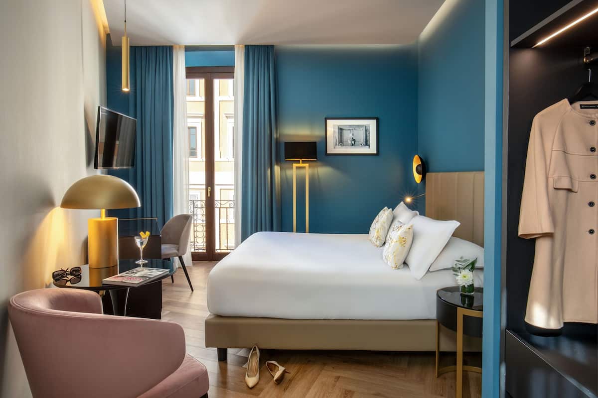Une chambre d’hôtel avec un grand lit, une télévision, un bureau avec une lampe, une chaise et un porte-manteau.