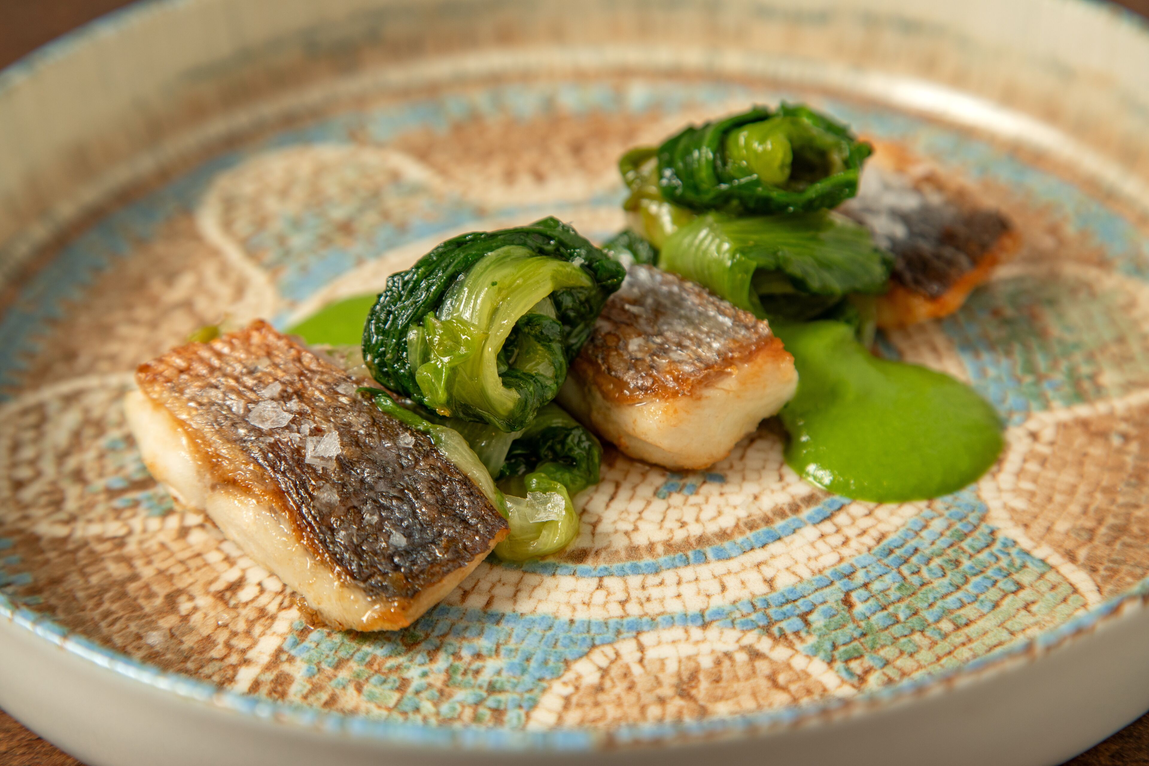 A plate with seared fish and green vegetables, possibly bok choy, on a patterned ceramic plate.