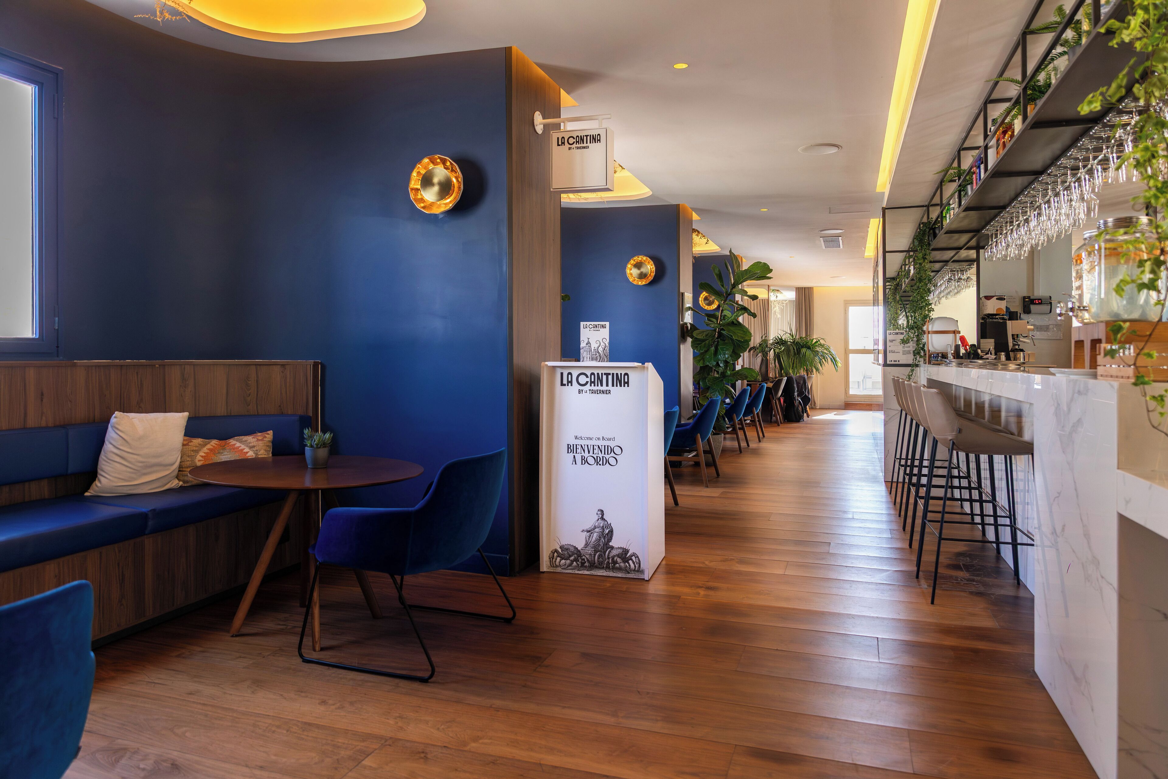 Un área de bar moderna con suelo de madera, asientos azules y una barra con vasos.