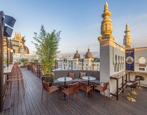 Terraza en la azotea con suelo de madera, mobiliario y vistas a edificios históricos.