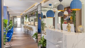 Ein modernes Interieur mit einer Rezeption, blauen Stühlen, Topfpflanzen und einer Bar mit Regalen und Hängeleuchten.