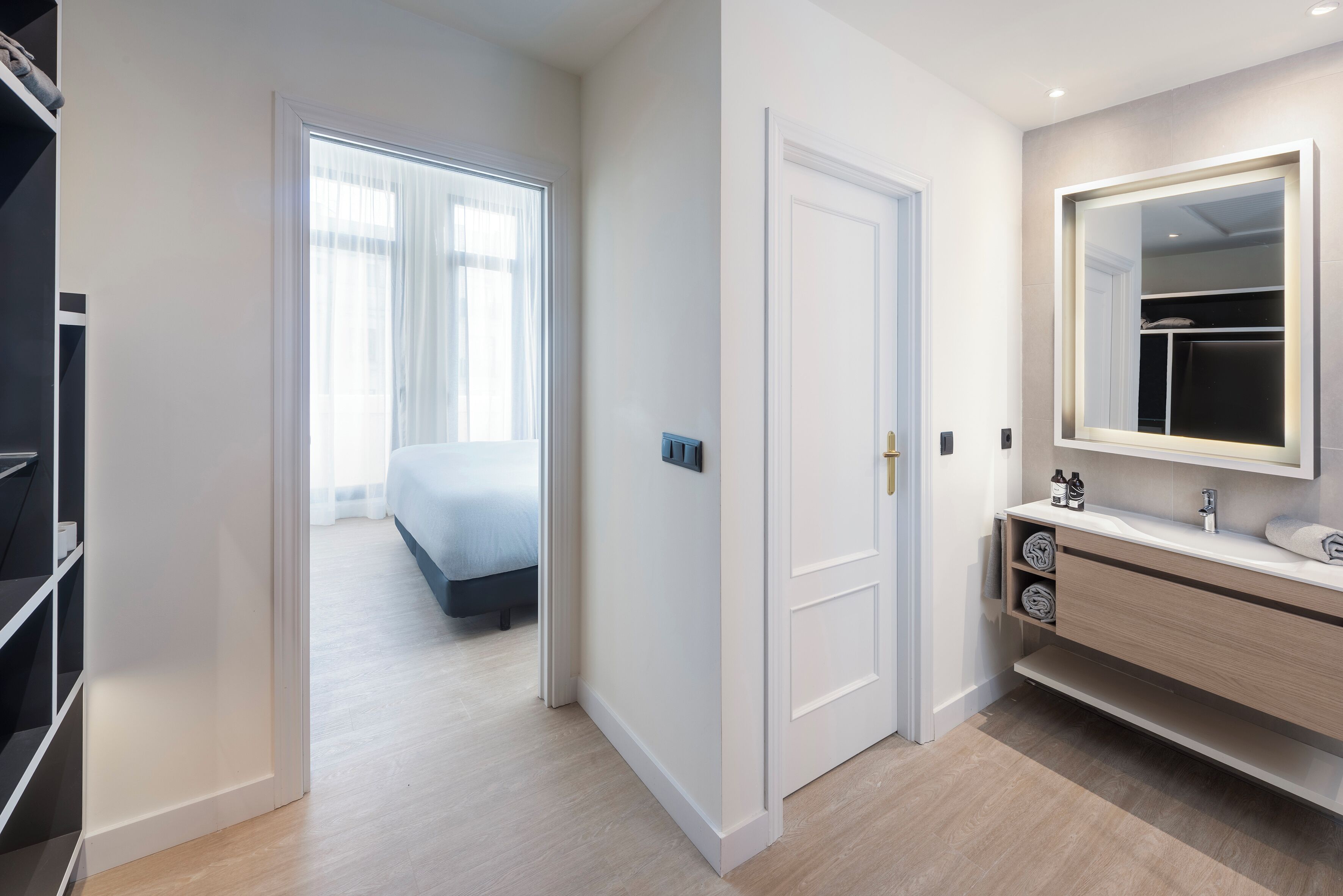 Quarto de hotel moderno com closet espaçoso, banheiro com espelho grande e cama com vista para a cidade.