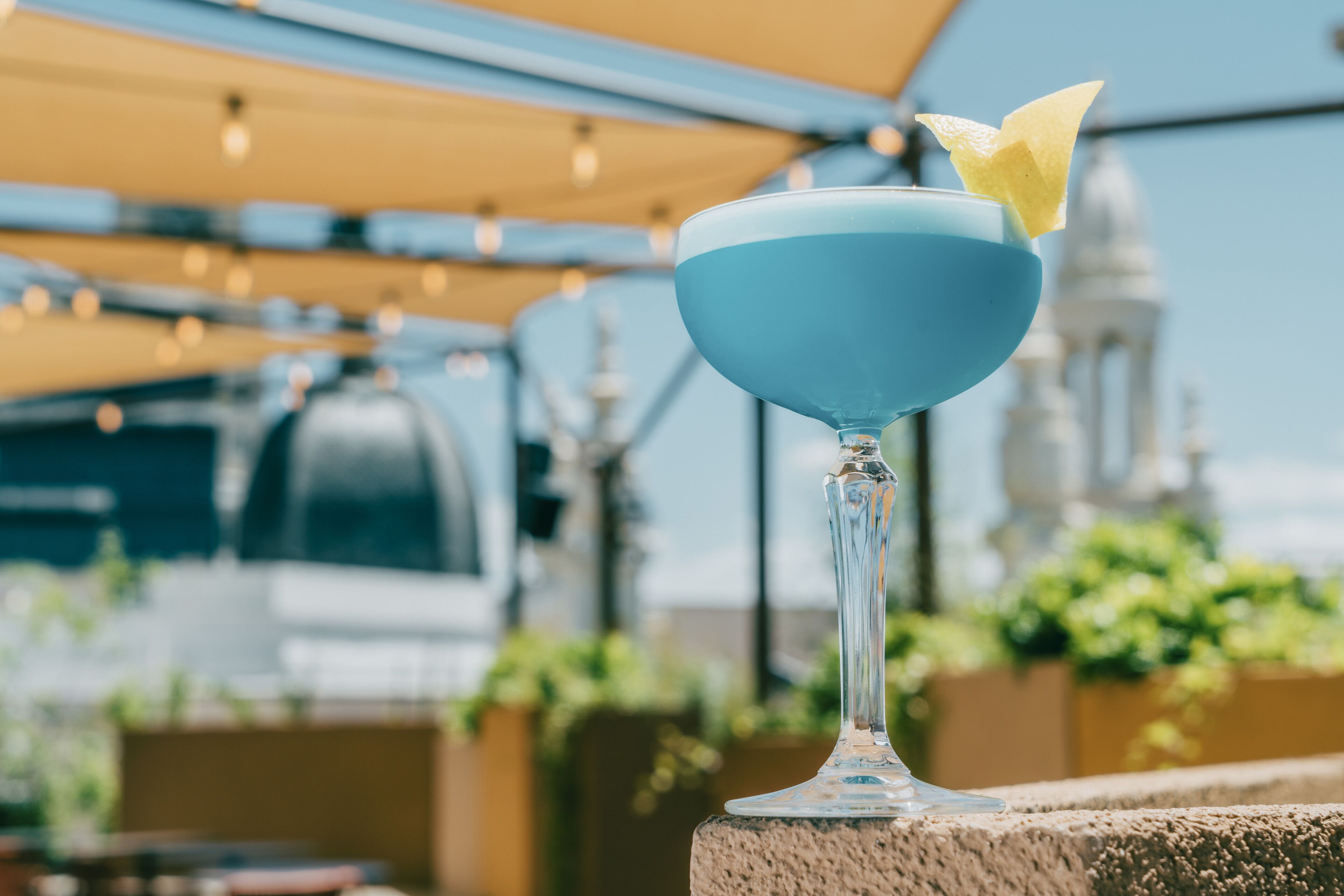 Um copo de cocktail com líquido azul e um enfeite numa varanda.
