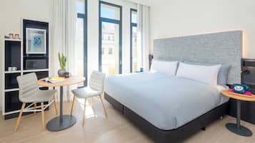 Una habitación de hotel moderna con una cama grande, un escritorio con silla, una mesita y una estantería.