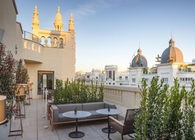 A rooftop terrace with outdoor seating, including a sofa and round tables, overlooking a cityscape with distinctive architecture and domed buildings.