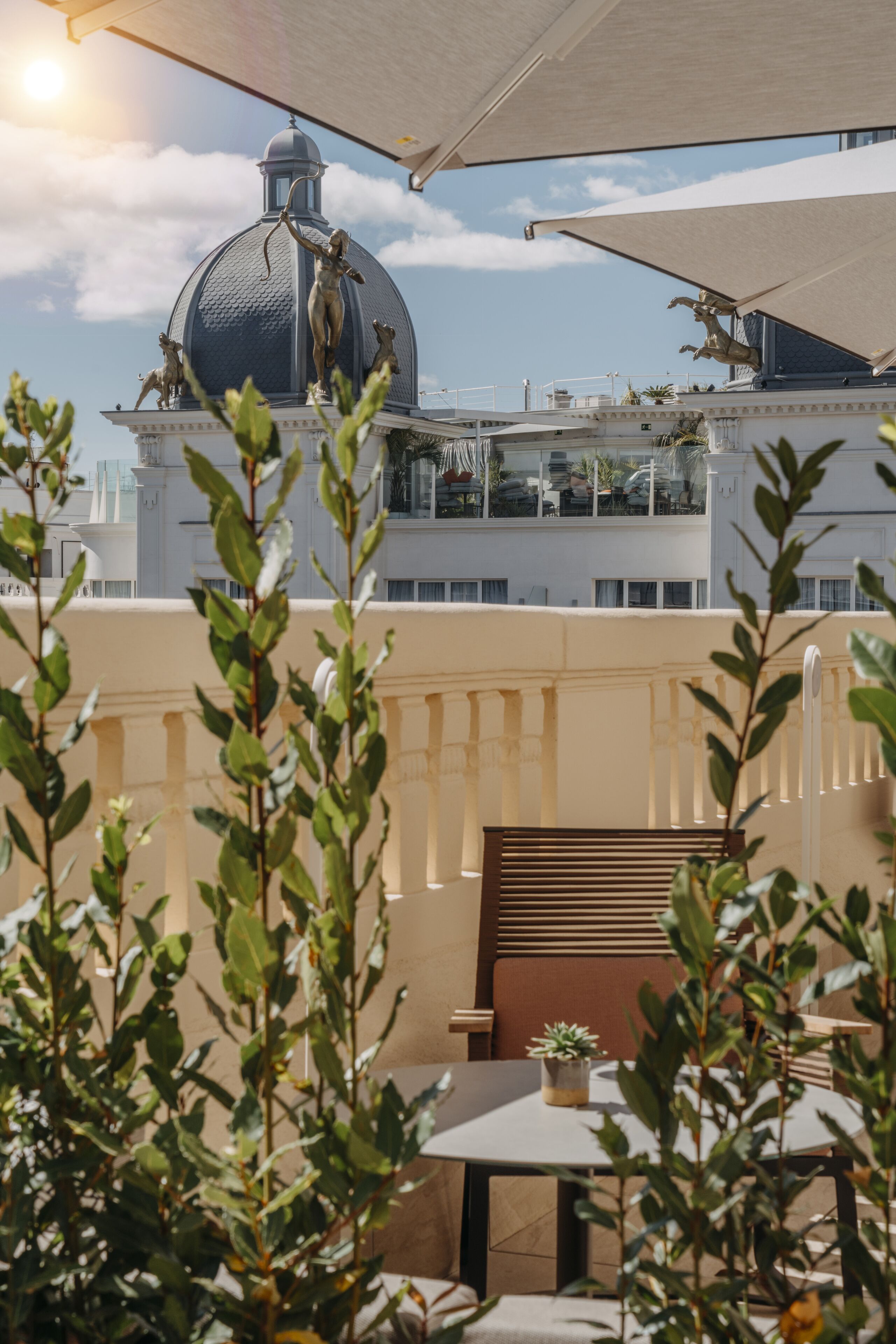 A terrace with a table and chairs, overlooking a building with a dome and statues.