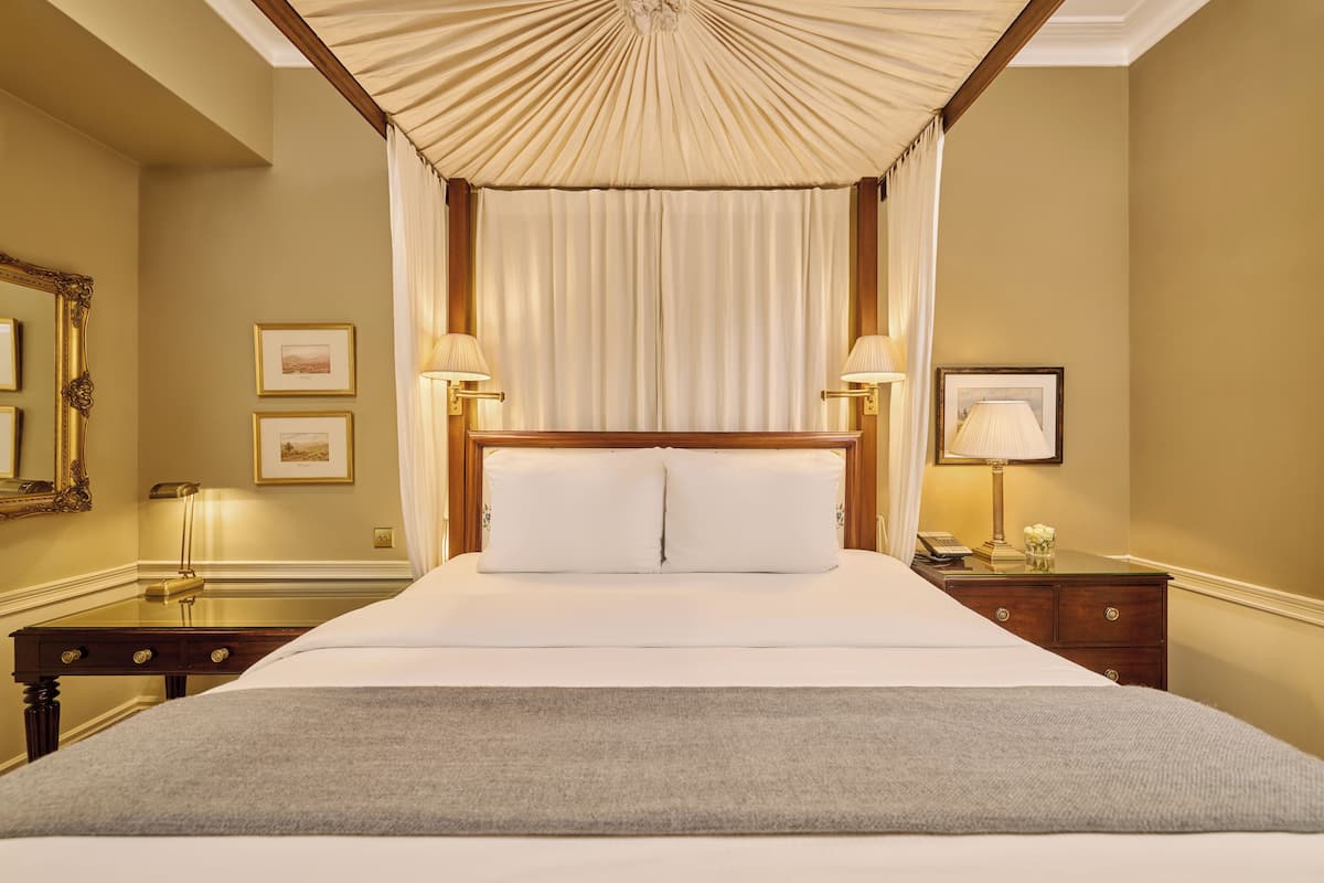 A large bed with a canopy, two bedside lamps, a nightstand, and framed pictures on the wall.