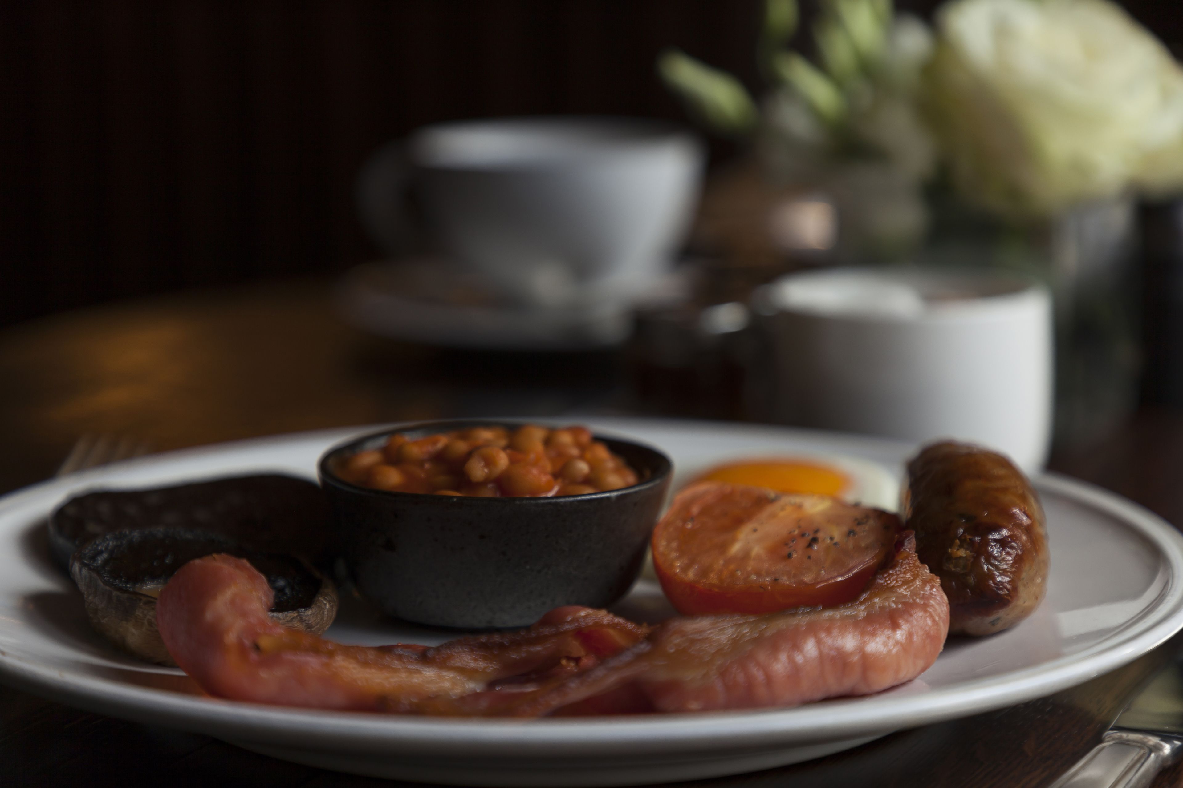 Un plato con tocino, salchichas, frijoles y tomate.