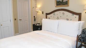 A neatly made bed with white linens, a wooden headboard with floral patterns, a bedside table with a lamp, and a painting on the wall.
