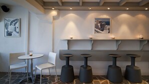 A modern interior with a stone floor, white chairs, and a bar area with stools and candles. - Regina Mare Adults Only (Santorini)