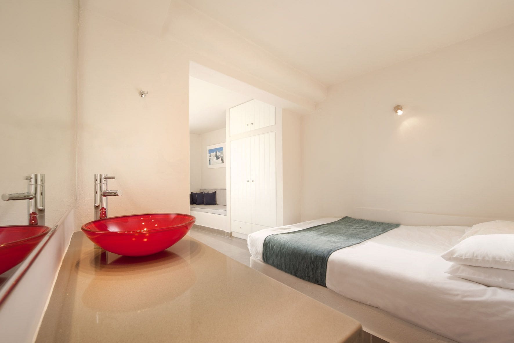 A modern hotel room with a large red bowl sink, a bed with white linens, and a view of the hallway.