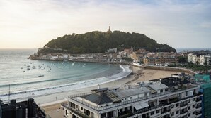 A coastal cityscape with a prominent hill, beach, and marina.