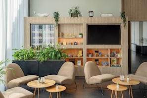 A modern lobby with a wooden reception desk, comfortable seating, and a large TV screen. - INNSiDE by Meliá San Sebastian Orly (San Sebastián)