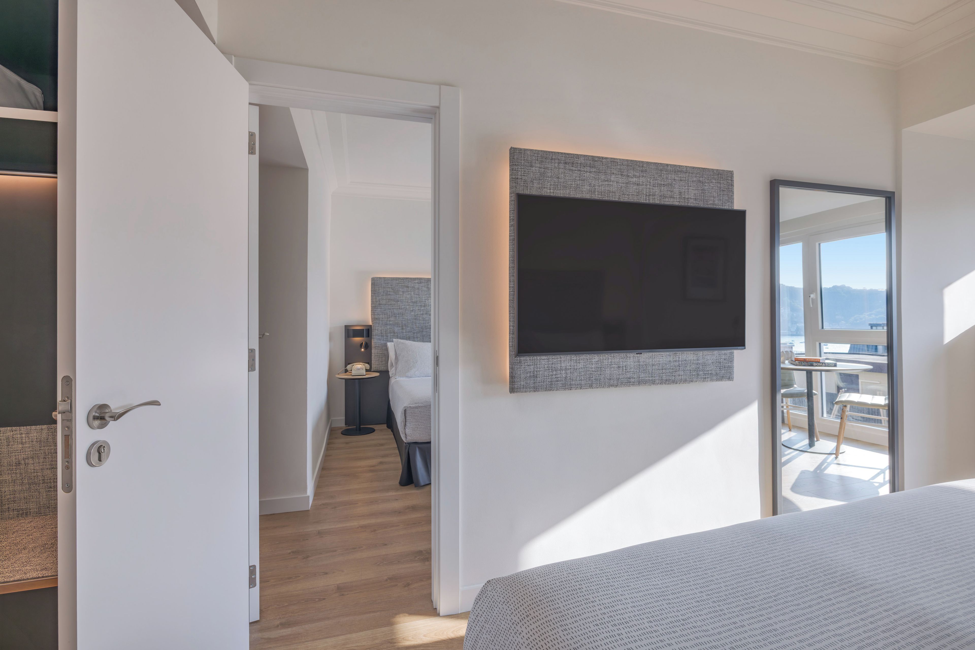 Habitación de hotel moderna con una cama grande, un televisor de pantalla plana en la pared y un balcón con vistas.