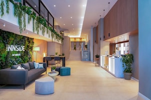 Un vestíbulo moderno con mostrador de recepción, zona de estar, escalera y una pared con plantas.