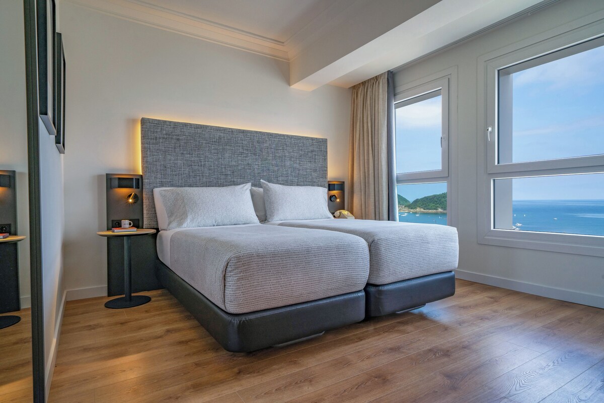 Une chambre moderne avec un grand lit, deux tables de chevet et une vue sur la mer.