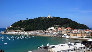 A coastal town with a prominent hilltop church, a marina with boats, and a mix of historic and modern buildings.