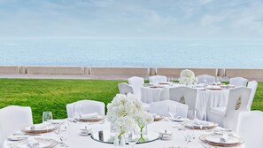 A table set for a formal outdoor dining event with a view of the sea.