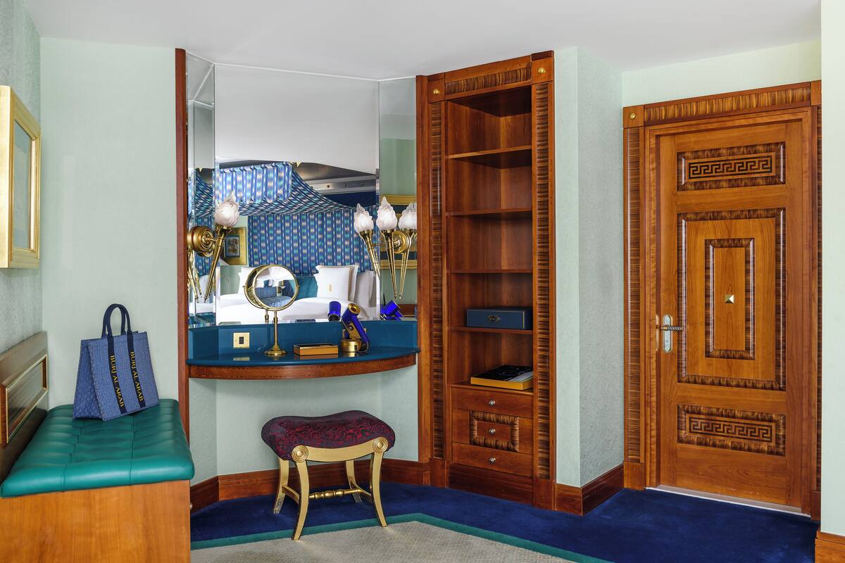 Ein Zimmer mit einer hölzernen Bank, einem Schreibtisch mit Spiegel, einem Schminktisch mit Spiegel, einem Holzschrank und einer Tür mit dekorativer Verzierung.