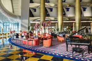 A grand lobby with a grand piano, red and white patterned sofas, and a checkered floor.