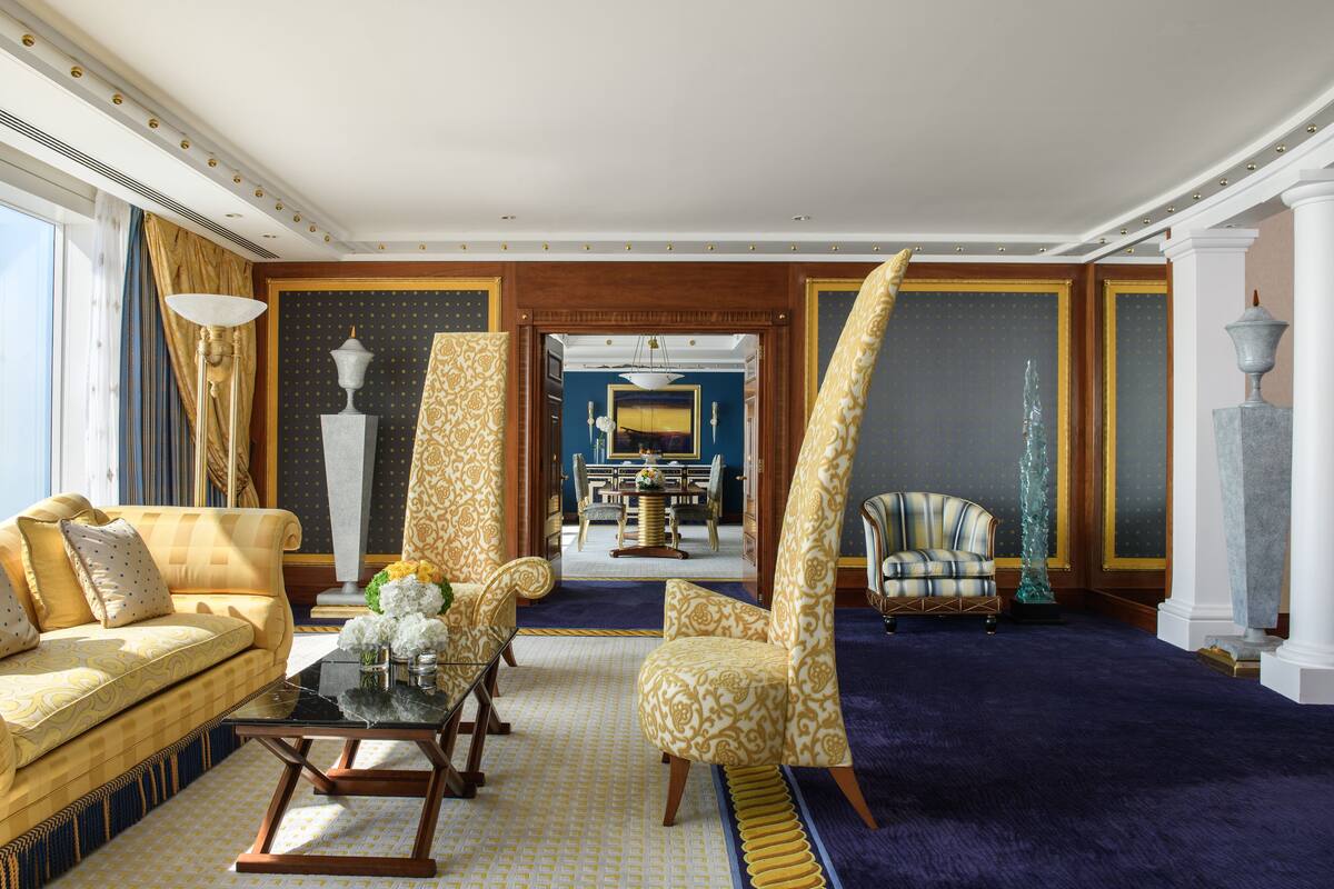 Ein luxuriöses Zimmer mit einer bequemen Couch, einem gemusterten Sessel, einem Essbereich und einem blauen Teppich.