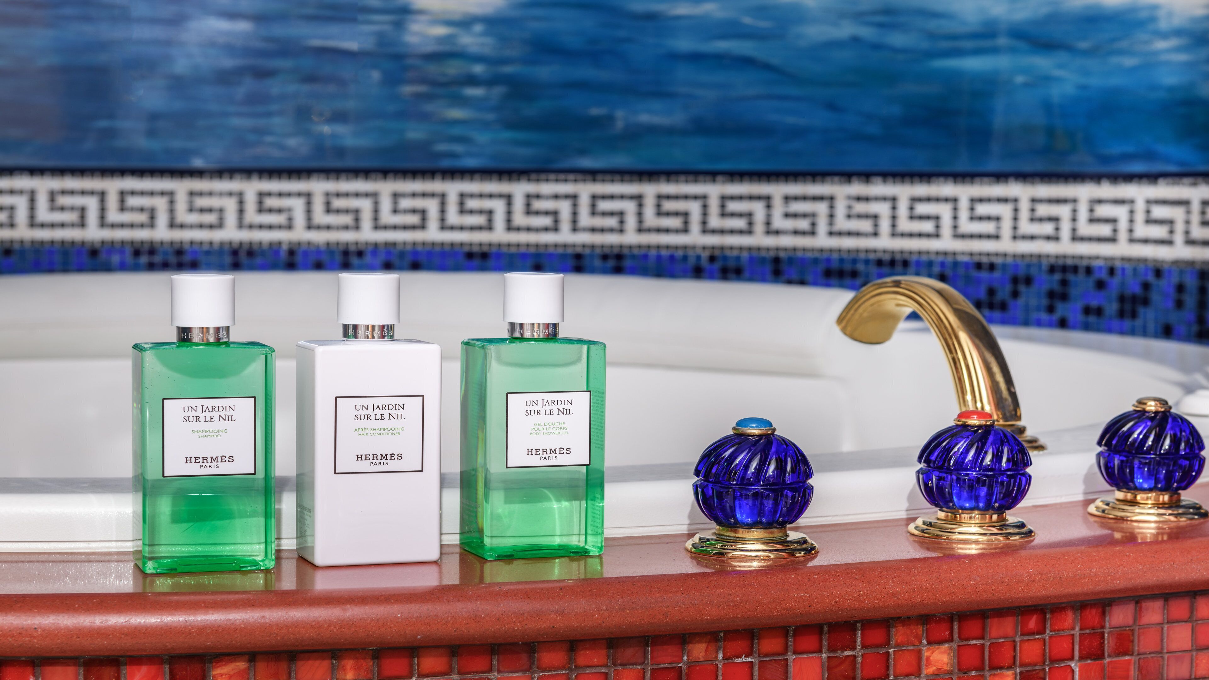 Trois flacons d’après-shampoing et de shampoing de la marque Hermès Paris sont posés sur le comptoir d’une salle de bain.