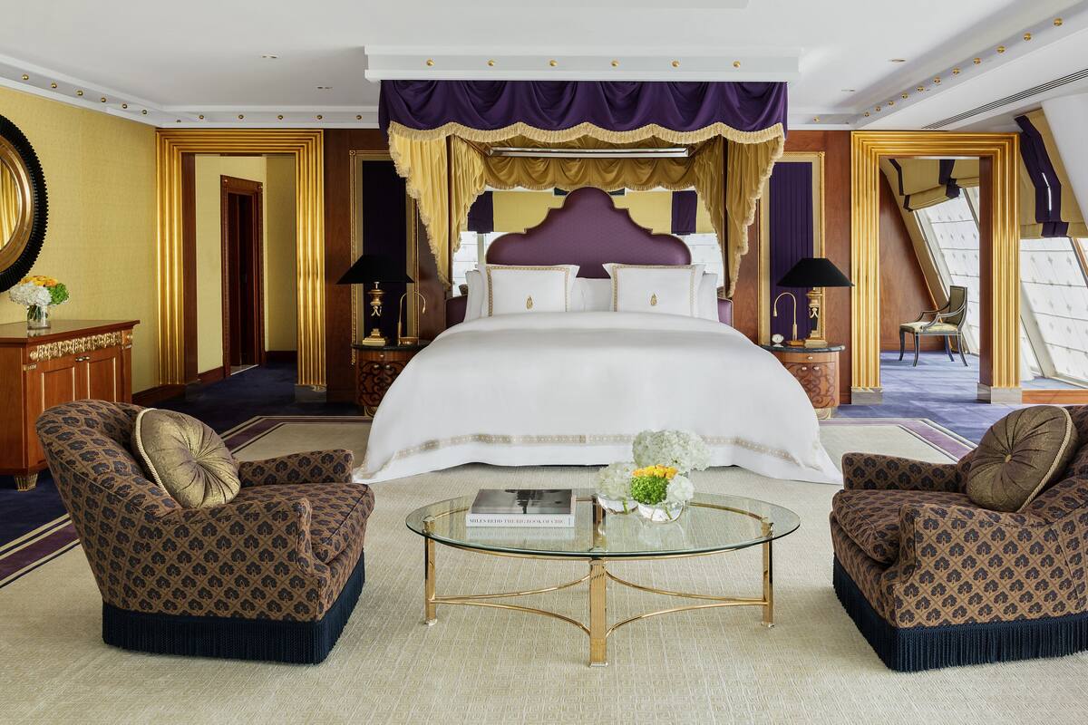 Ein luxuriöses Schlafzimmer mit einem großen Bett, zwei Sesseln, einem Glastisch und einem Spiegel an der Wand.