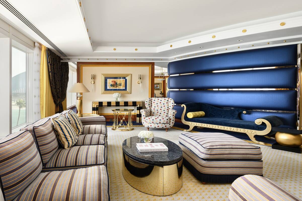Ein luxuriöses Wohnzimmer mit einer großen Couch, einem gemusterten Hocker, einem runden Couchtisch und einem blau gepolsterten Sofa.