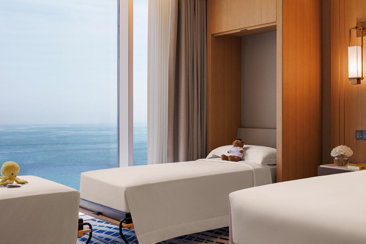 A hotel room with two beds, a view of the ocean, a plush octopus toy on the left bed, and a teddy bear on the right bed.