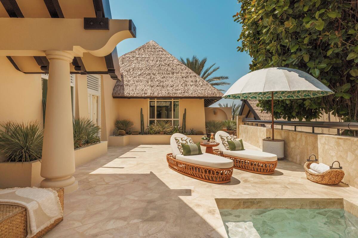 Un patio con mobiliario de mimbre, una piscina y un edificio con techo de paja.