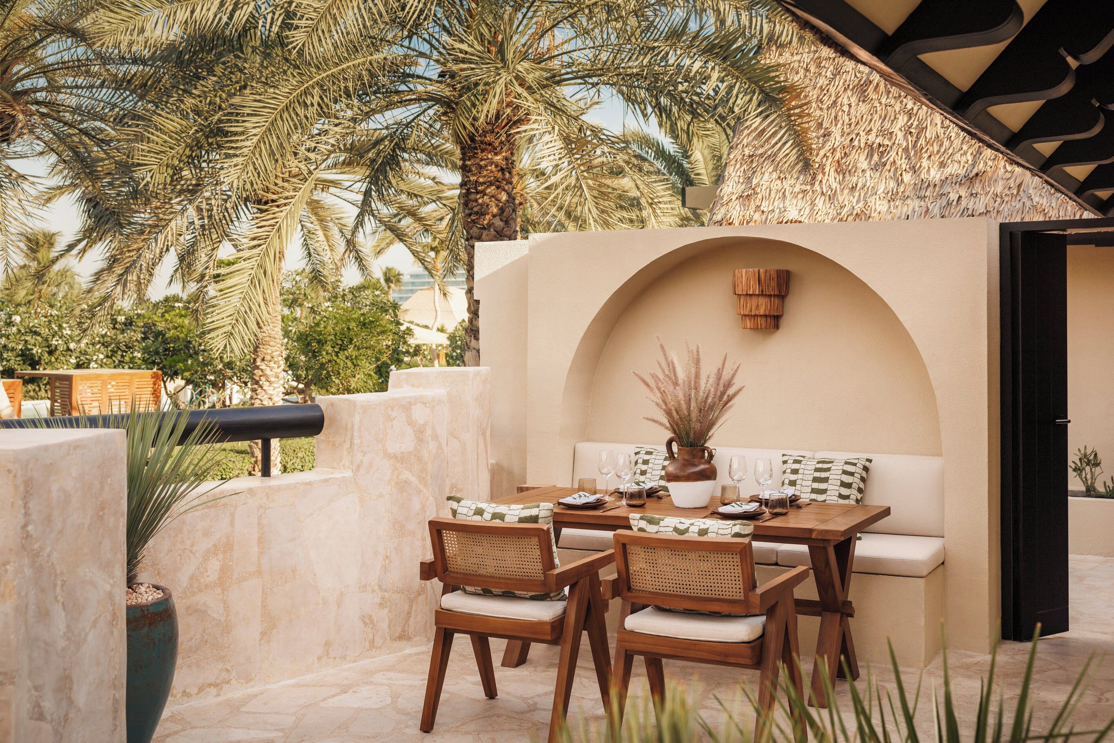 An outdoor patio with a wooden table and chairs, a cushioned bench, and a decorative wall.