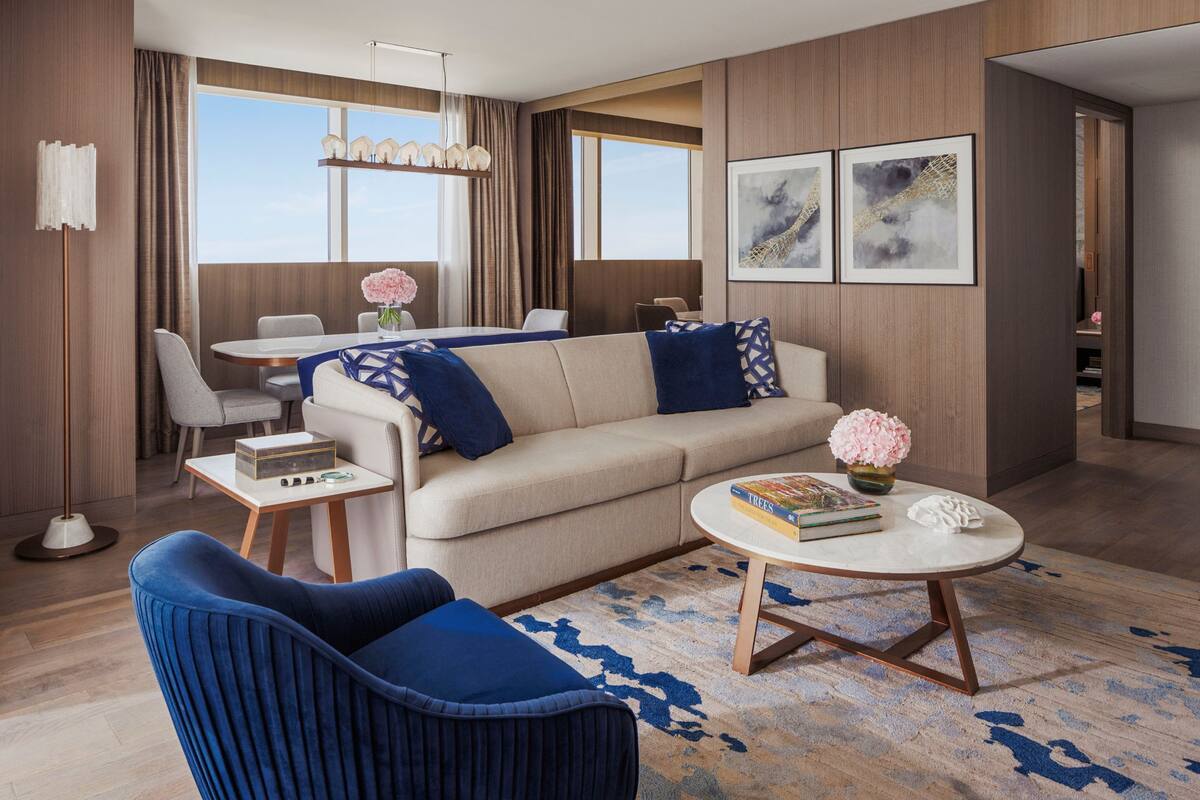 Una sala de estar moderna con sofá, mesa de centro y sillón azul. Hay un comedor con mesa y sillas, y obras de arte en las paredes.