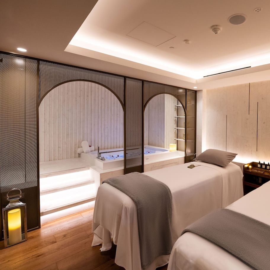 A modern hotel room with two beds, a bathtub, and a view of a spa area.