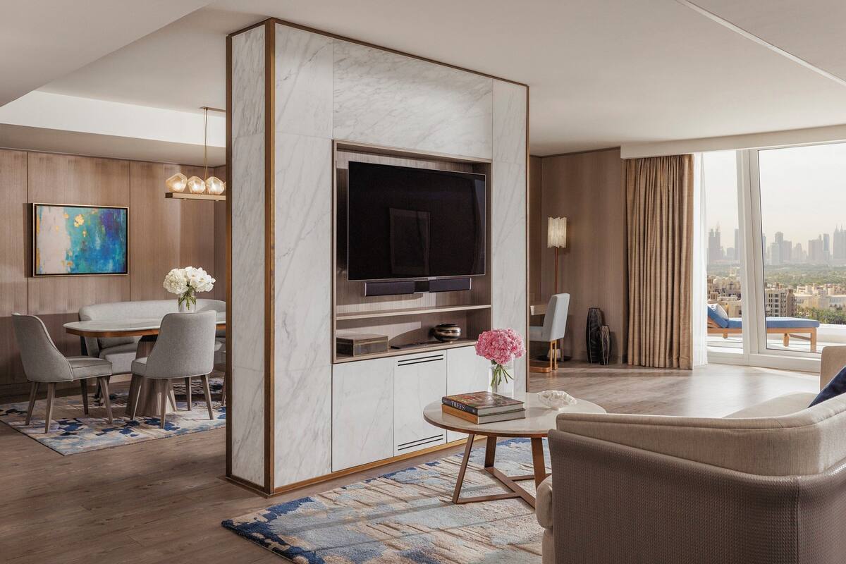 Una sala moderna con televisor de pantalla plana, un comedor con mesa y sillas, y un ventanal con vistas a la ciudad.