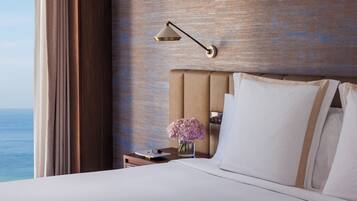 A hotel room with a large bed, a nightstand with a lamp, and a view of the ocean.