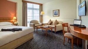 A hotel room with a bed, two armchairs, a sofa, a coffee table, a desk with a laptop, a lamp, and a TV on the wall. - J5 Hotels - Port Saeed (Dubai)