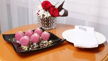 Una mesa con una bandeja de macarons rosas, una jarra de cristal con rosas rojas y una servilleta blanca doblada.