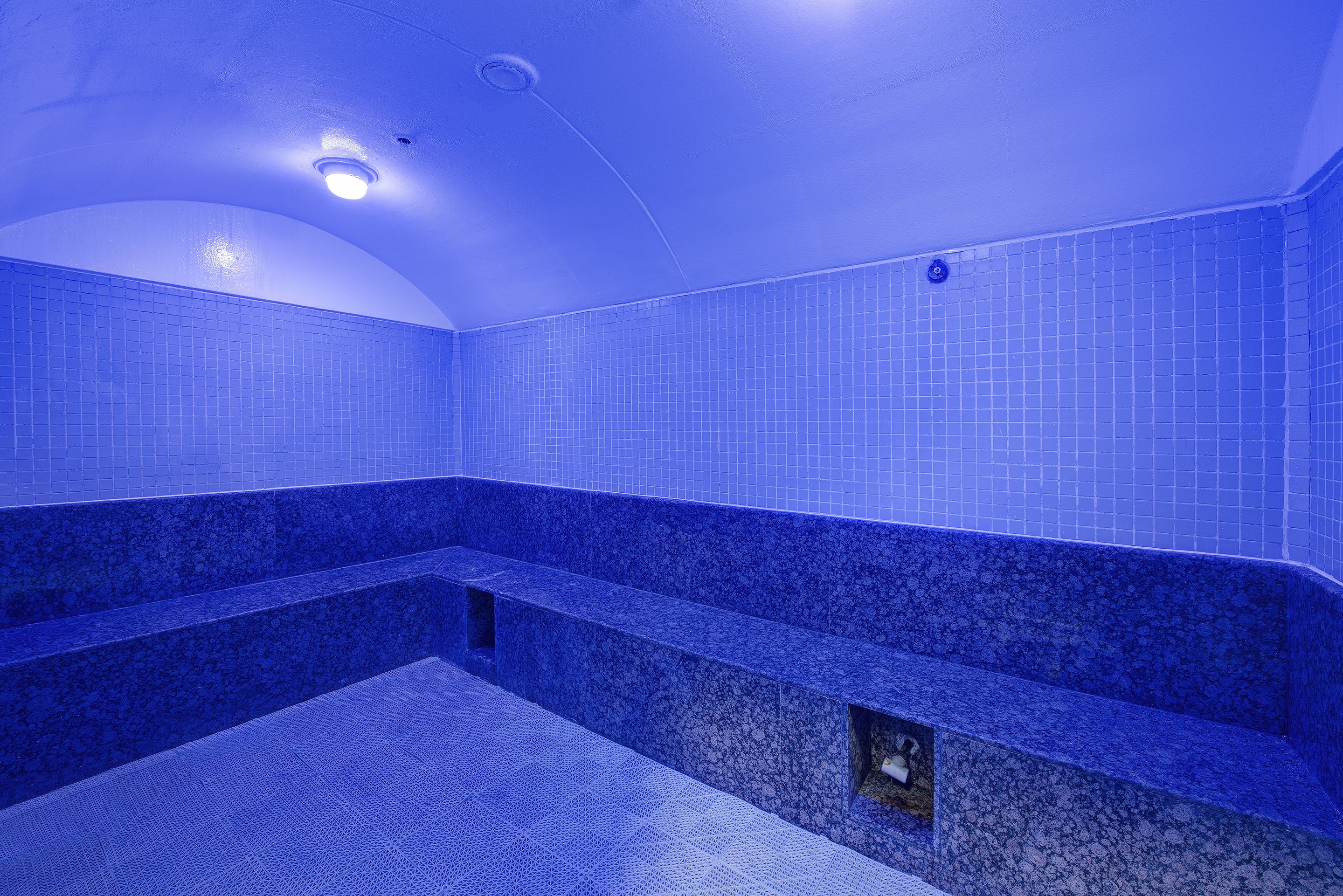 Un espacio interior con piscina de azulejos azules y escalones que conducen a una zona de estar.