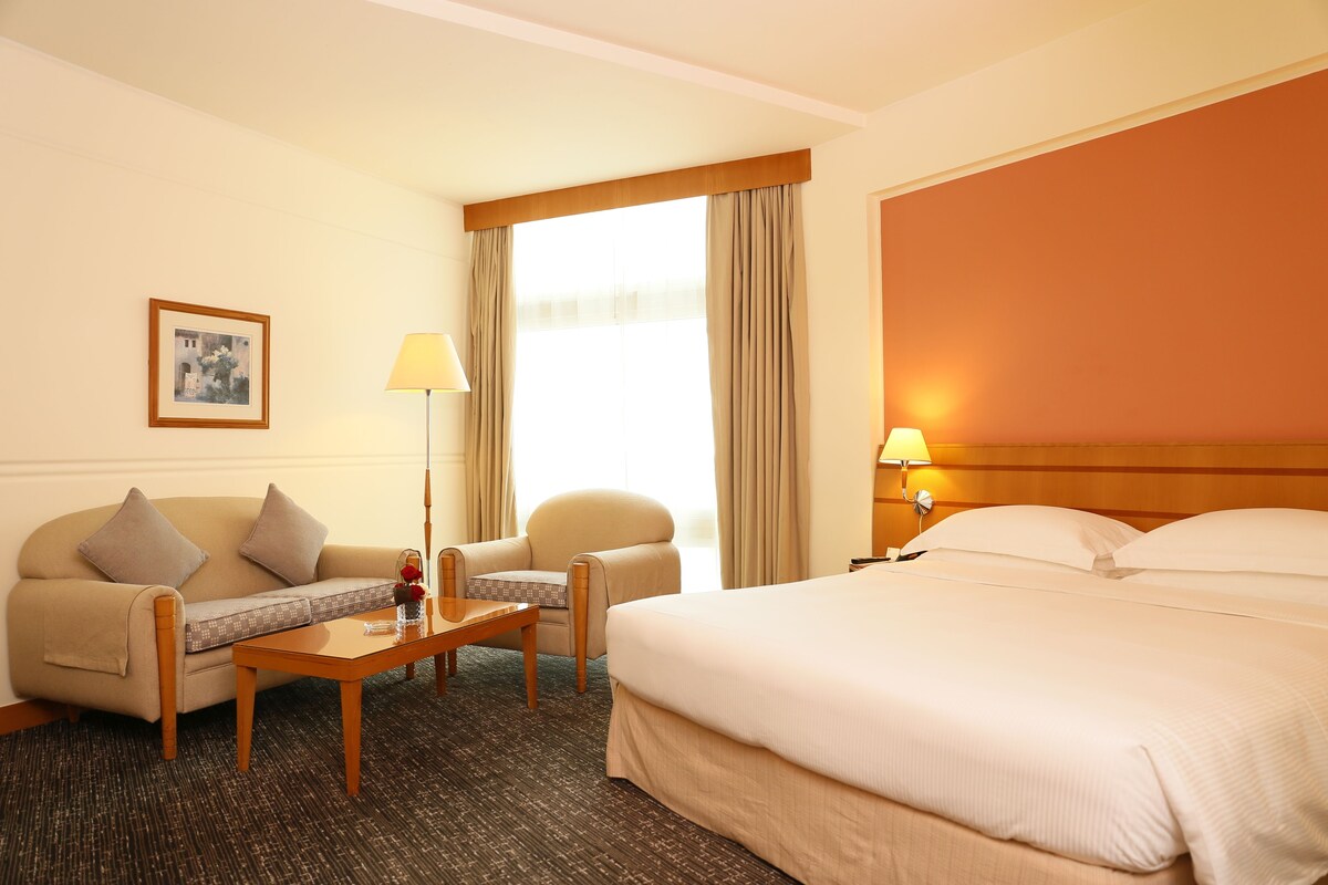 A hotel room with a bed, a sofa, a chair, a table, and a lamp.