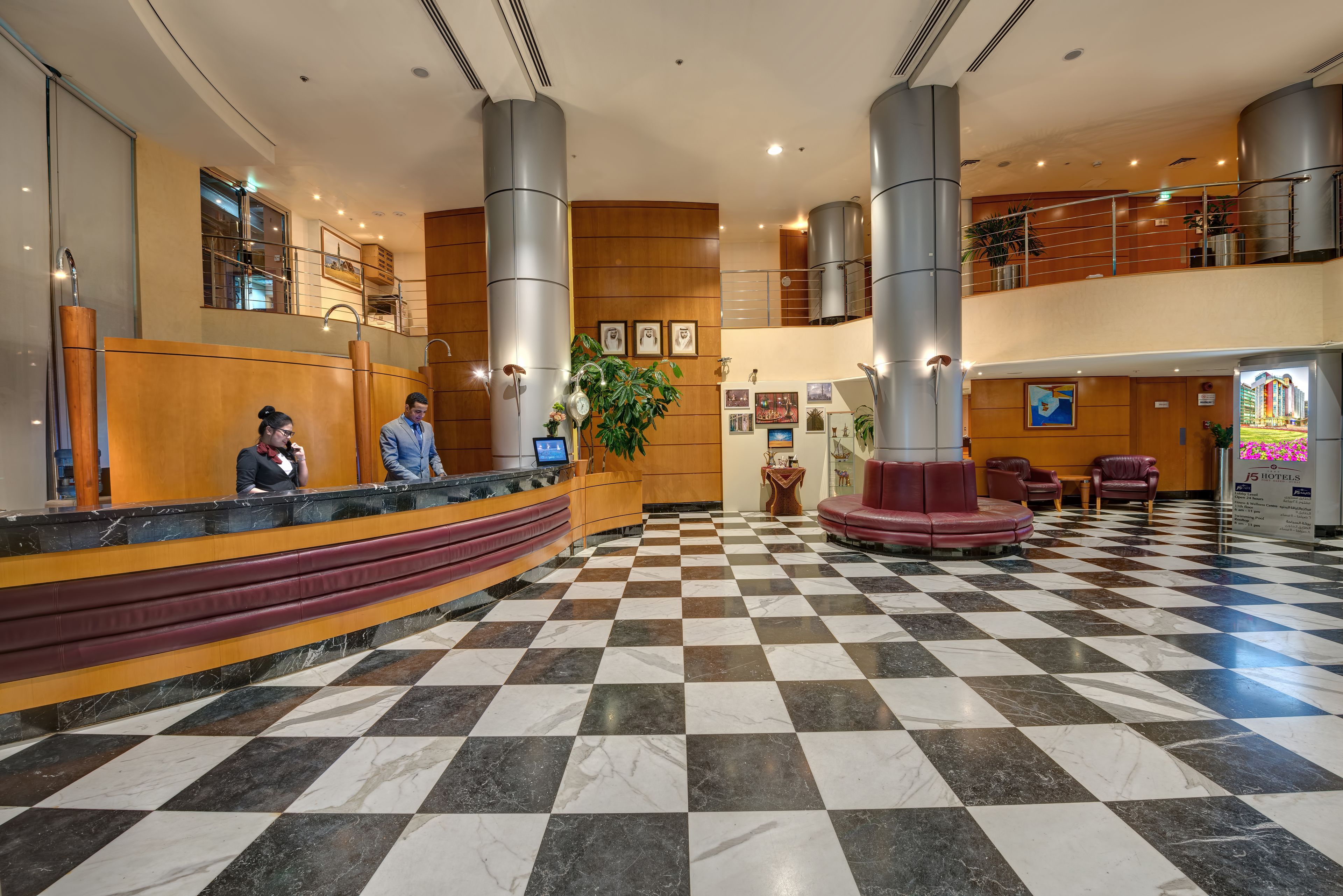 A hotel lobby with a checkered floor, a reception desk, and a staircase to the upper level.
