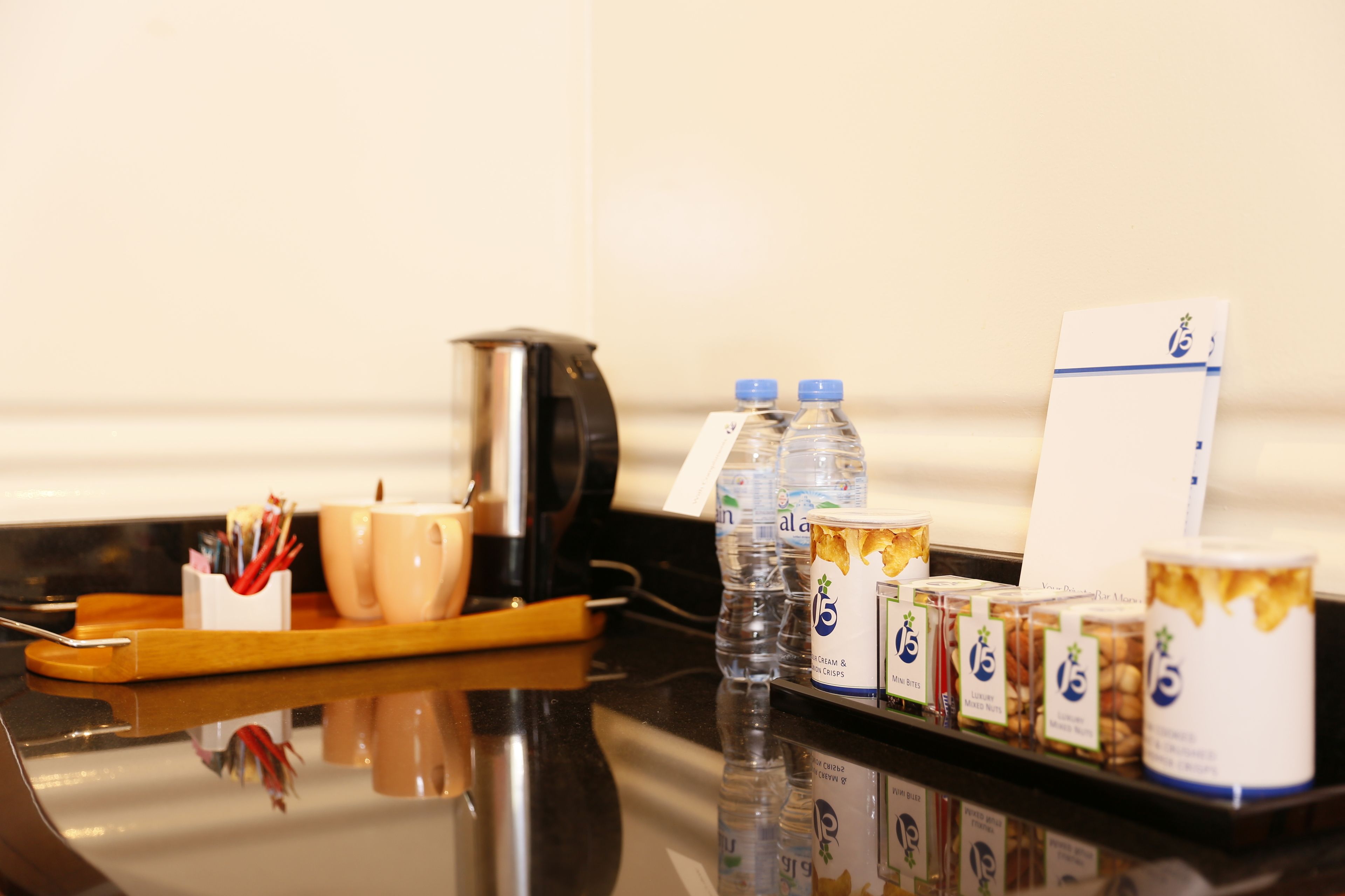 A hotel room's breakfast tray with cups, a kettle, water bottles, and packaged snacks.