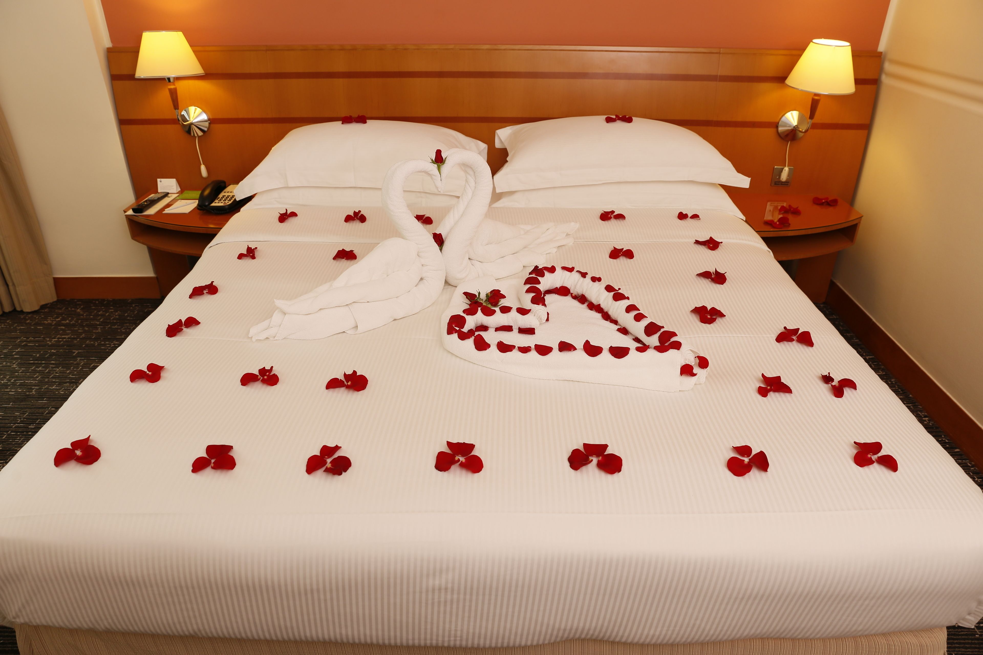 Quarto de hotel com cama bem arrumada, duas luminárias de cabeceira, um telefone e uma mesa de cabeceira.